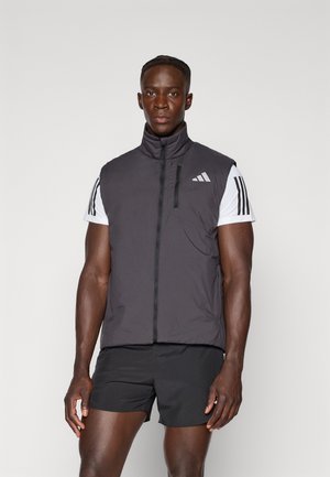 Black sleeveless vest with high collar, front zip, and Adidas logo; paired with a white shirt featuring black stripes and black shorts.