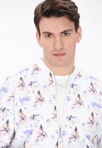 Lichte zip-up jack met een witte achtergrond, met een kleurrijk patroon van palmbomen en driehoeken in paarse, roze en blauwe tinten.