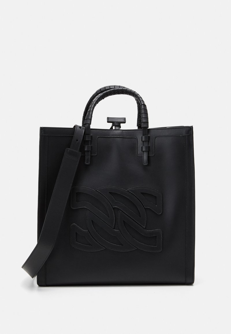 Black leather tote bag with a structured design, featuring a prominent embossed logo, stitched details, and a removable strap for versatility.