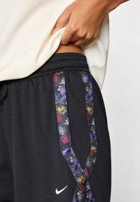 Μαύρο παντελόνι φόρμας με πλαϊνή φλορά λωρίδα. Κατασκευασμένο από υλικό με υφή και ελαστική μ έση. Λογότυπο Nike στο μπροστινό μέρος.