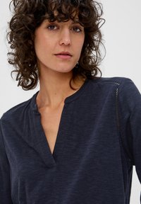 Marineblaue Bluse mit tiefem V-Ausschnitt und leichtem Stoff. Verfügt über aufwendige Nähte an den Schultern, die ein strukturiertes Design schaffen.