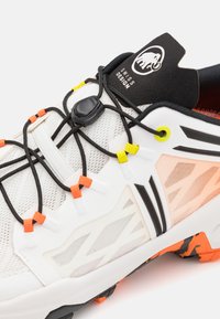Biała sportowa buty z przewiewnym siateczkowym wierzchem, czarnymi akcentami, regulowanymi elastycznymi sznurówkami i kolorowymi detalami. Gruba, teksturowana podeszwa.