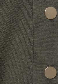 Tessuto a maglia verde scuro con una texture a coste; presenta bottoni metallici lisci come dettagli.