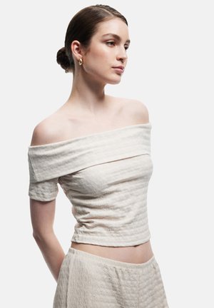 Haut léger couleur beige clair à épaules dénudées avec un tissu texturé et froissé. Design ajusté, manches courtes et longueur cropped.