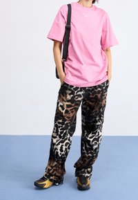 Rosa bomulls-t-shirt med vitt logotyp, ihopparad med svarta och bruna djurmönstrade byxor. Svarta sneakers med gula accenter fulländar outfiten.