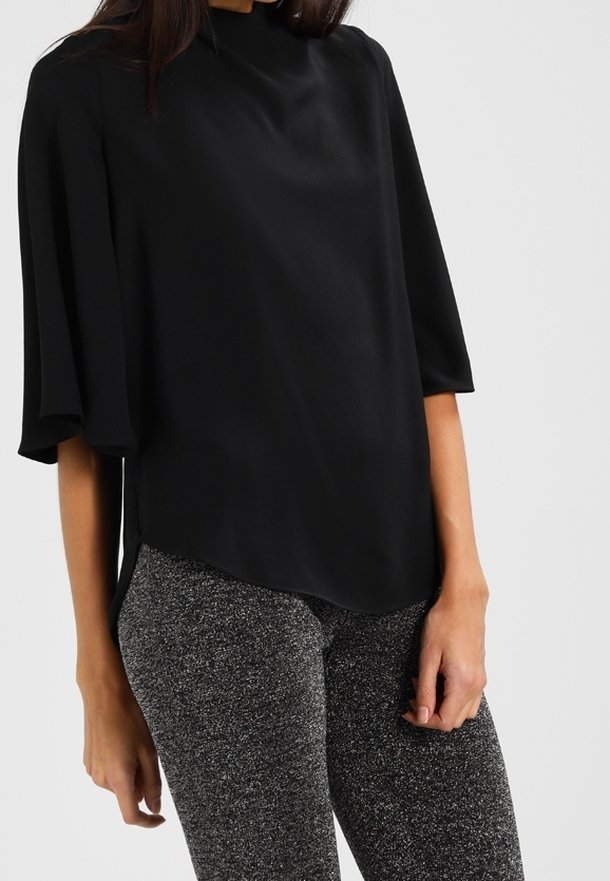 Blouse noire à manches courtes, col montant et texture lisse ; associée à des leggings gris étincelants.