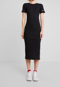 Robe midi noire côtelée avec des manches courtes, un col rond et un ourlet arrondi. Portée avec des baskets blanches avec des accents rouges.