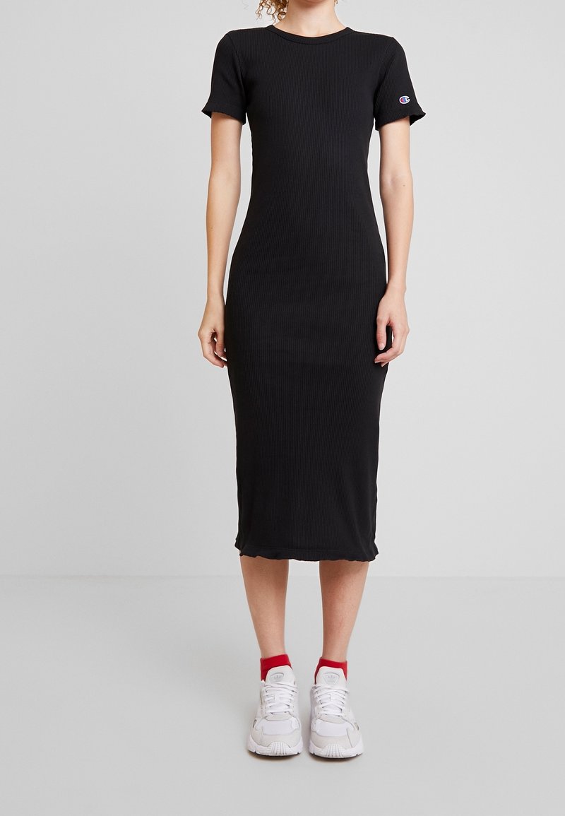 Robe midi noire côtelée avec des manches courtes, un col rond et un ourlet arrondi. Portée avec des baskets blanches avec des accents rouges.