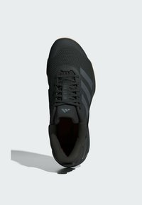 Black athletic shoe with mesh upper, prominent three-stripe design in gray, rounded toe, and textured sole for grip.