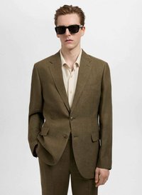 Sacou texturat maro cu o pereche asortată de pantaloni. Purtați cu o cămașă bej deschis și ochelari de soare negri. Design simplu, croit.