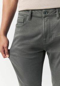 Hallid denim püksid slim fit lõikega, viie taskuga, nööbi ja tõmblukuga, ning peente õmblustehnikatega. Sile tekstuur ja veniv materjal.