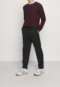 Burgundský pletený svetr s okrouhlým výstřihem, černé kalhoty se stahovací šňůrkou v pase a šedé tenisky s třemi světle modrými pruhy.