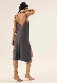 Fioletowa, bezrękawnikowa sukienka z głębokim dekoltem na plecach, gładka tekstura, do kolan z bocznym rozcięciem dla swobody ruchów.