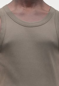 Khaki geribd tanktop met een ronde halslijn en brede schouderbanden. De stof heeft een getextureerde, zachte afwerking.