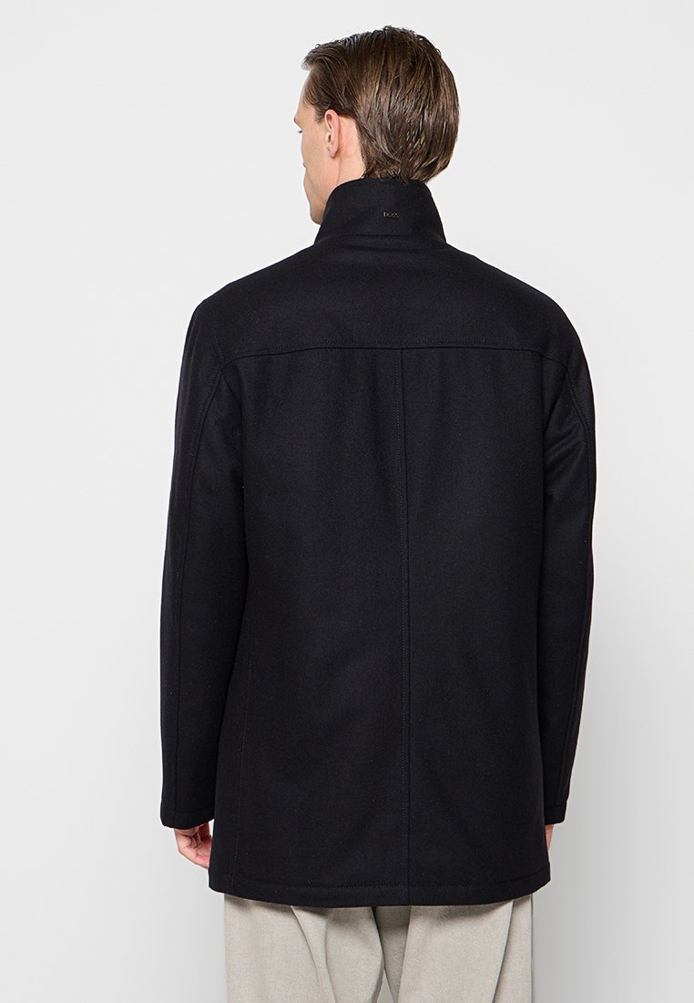 Manteau en laine noir avec un col haut. Comporte des lignes épurées, une silhouette ajustée et des détails de couture subtils le long des coutures.