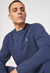 Navyblauwe sweatshirt met lange mouwen en een ronde halslijn. Voorzien van een wit chevronlogo op de borst. Zachte, geribbelde manchetten en zoom.