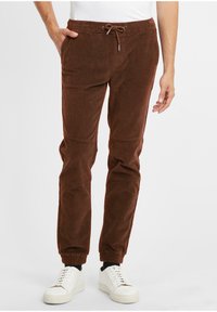 Brown corduroy jogger pants with elastic cuffs, adjustable drawstring waistband, and side pockets, paired with white sneakers.