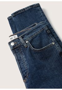 Jean en denim bleu foncé avec une coupe slim, détails de couture visibles et une étiquette sur la ceinture. Comprend un design de poche standard et une fermeture par bouton.