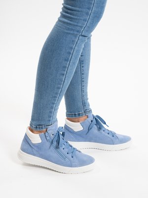 Person, die hellblaue high-top Sneaker aus Wildleder mit weißen Sohlen und Reißverschlüssen trägt, kombiniert mit eng geschnittenen blauen Jeans.