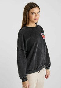 Sweat-shirt en polaire noire avec un col rond, des poignets froncés et un imprimé graphique représentant des cerises en rose et vert.