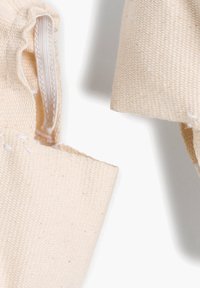 Tessuto in cotone di colore beige naturale con cuciture visibili e cerniera nascosta. La trama è tessuta e robusta, adatta per vari utilizzi.