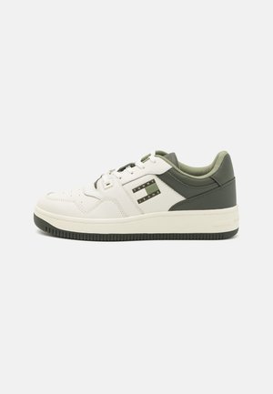 Zapatilla blanca de cuero con acentos en verde oliva, que cuenta con un collarín acolchado, puntera redonda y una suela de goma texturizada. Detalle de logo plateado en el costado.