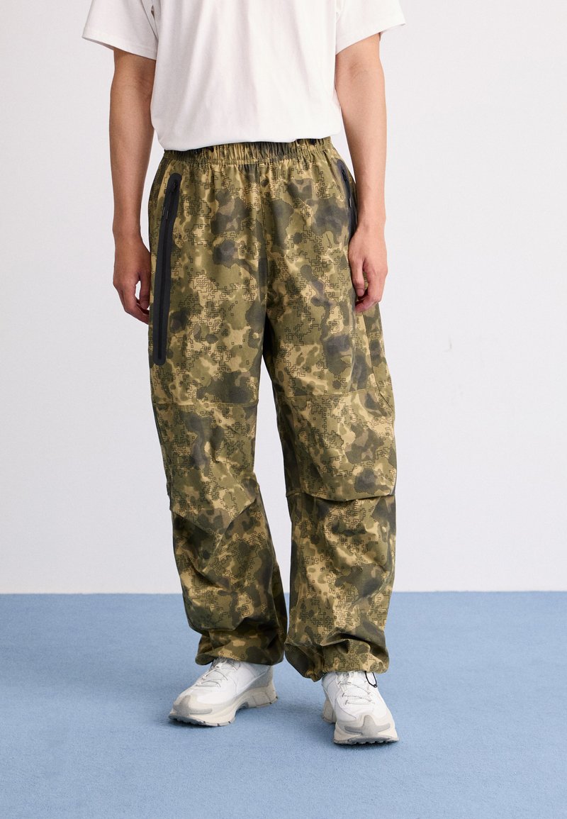 Camo patterned cargo pants in green tones, featuring an elastic waistband, side zip pockets, and slightly tapered legs.