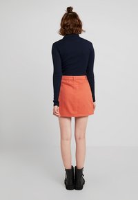 Falda de mezclilla en un brillante color naranja, con una cintura ajustada y forma de A. Combinada con un suéter de cuello alto negro ajustado y botas negras hasta el tobillo.