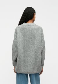 Gray knitted sweater with a textured pattern and a round neckline. Finished with loose-fitting sleeves and a longer back hem.