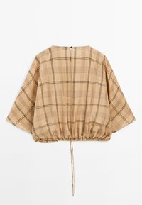 Beige geruite blouse met brede mouwen, een geboetseerde taille en een rits aan de achterkant. Het materiaal lijkt lichtgewicht met een zachte textuur.