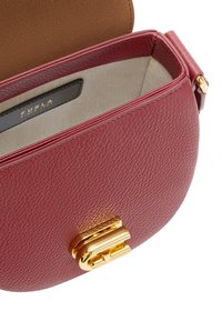 Červená kožená kabelka s jemným zrnem a béžovým interiérem, otevřenou klopou a zlatým zapínáním, ukazující černou etiketu s značkou Furla a textem uvnitř.