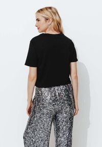 Haut noir à manches courtes associé à un pantalon large en sequins argentés brillants, présentant une surface texturée et une taille élastique.