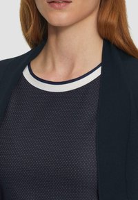 Il capo superiore di colore navy presenta un tessuto strutturato con piccoli punti a spillo, completato da un colletto a contrasto bianco e navy.