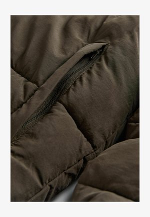 Donkergroen pufferjack close-up, met een gequilt ontwerp, een zichtbare zwarte rits en een gladde, iets glanzende textuur.