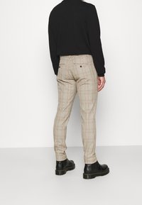 Béžové kárované kalhoty s úzkým střihem, vyrobené z texturovaného materiálu, s předními kapsami a středně vysokým pasem, kombinované s černými botami.