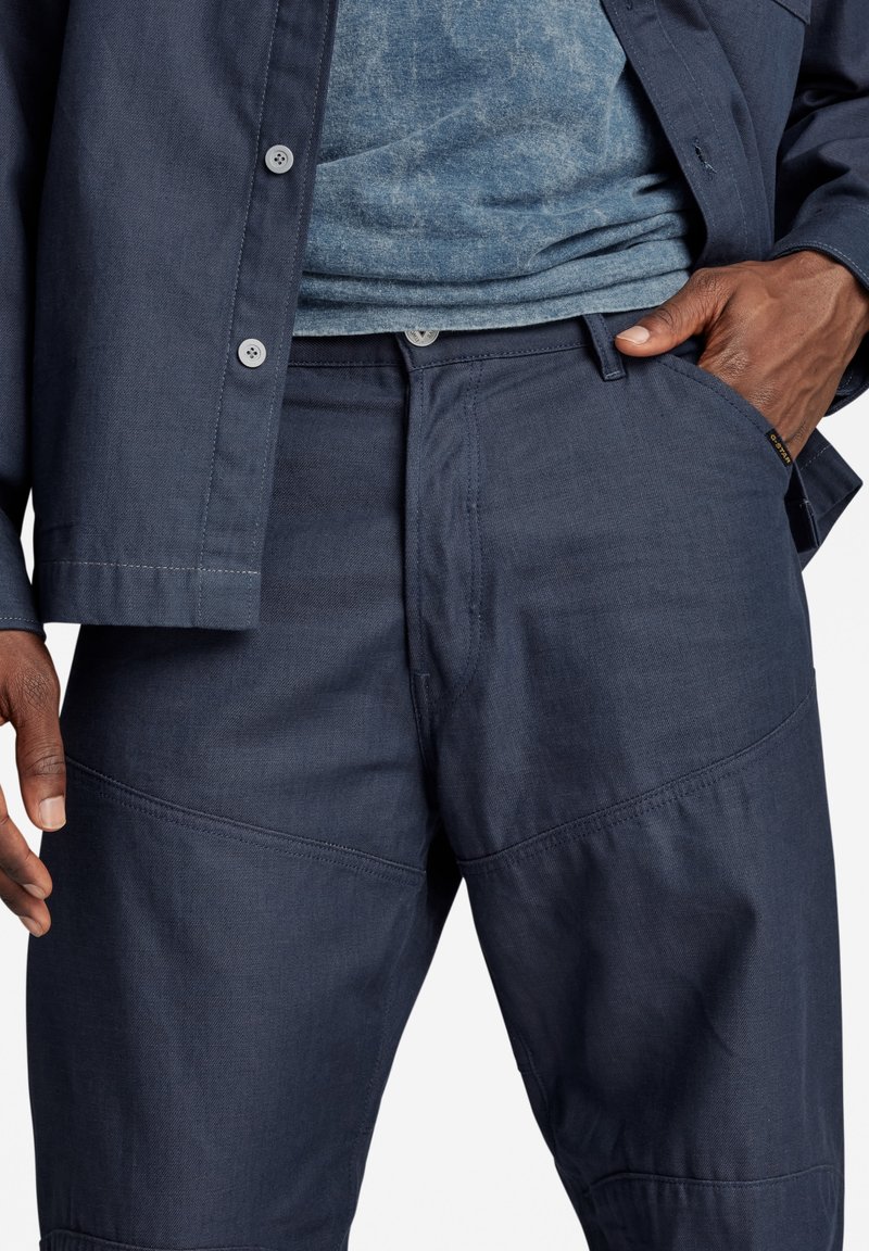 Donkerblauwe lichtgewicht stoffen broek met een gladde textuur, voorzien van zijzakken en paneelstiksel voor extra detail. Slanke pasvorm.