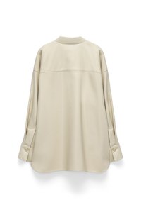 Cream-colored, long-sleeve shirt with a relaxed fit, featuring a button detail at the cuffs and a smooth, textured fabric.