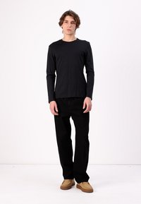 Sort langærmet skjorte lavet af blødt stof, parret med sorte bukser og brune sko med teksturerede såler. Minimalistisk design uden mønstre.