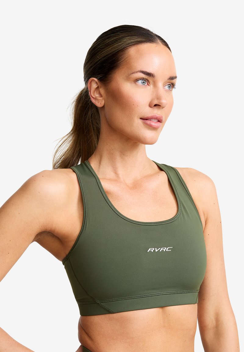 Olivgrön sportbh gjord av stretchigt material. Har en båtringning, breda axelband, och en liten vit logotyp på framsidan.