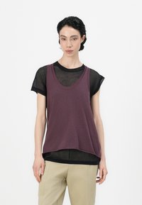 Paarse tanktop bovenop een doorzichtige zwarte t-shirt, met een ronde halslijn en een ontspannen pasvorm, gecombineerd met beige broeken.