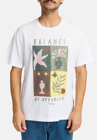 White cotton t-shirt featuring a geometric print with pastel colors, floral motifs, and text reading "BALANCE OF OPPOSITES" at the front.