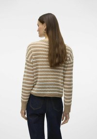 Pull en maille rayé beige et blanc avec une coupe ample, présentant un design texturé et des poignets côtelés, associé à un jean bleu foncé.
