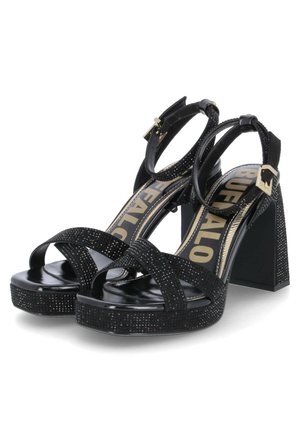 Black high-heeled sandals with a platform, featuring cross straps adorned with studs, an ankle strap, and a chunky square heel.