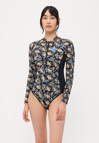Heldrakt med lange ermer har en svart base med blomstermønster i nyanser av gult, blått og oransje, komplettert med en frontglidelås.
