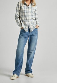 Rutet skjorte med knapper i lyseblå og creme, båret over falmede blå brede jeans, med struktureret stof og klassisk kravedesign.