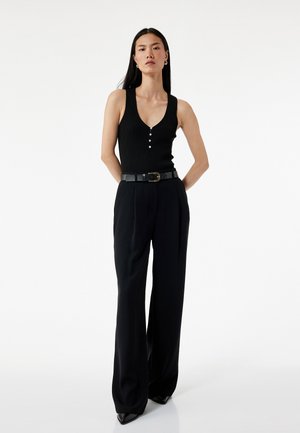 Top negro de canalé sin mangas con un profundo escote en V y tres botones, combinado con pantalones de pierna ancha negros de talle alto y un cinturón negro.