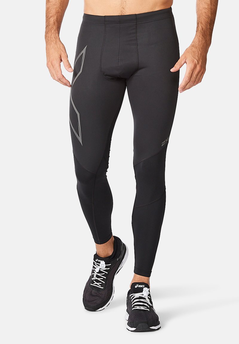 Sorte kompressions leggings med en tætsiddende design, der har grå detaljer og en glat, strækbar tekstur. Bæret med sorte atletiske sko.