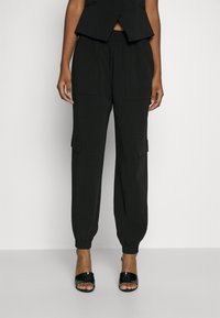 Pantalons cargo noirs avec des chevilles élastiques, comportant des poches latérales et une coupe décontractée. Fabriqués dans un tissu lisse avec une texture subtile.