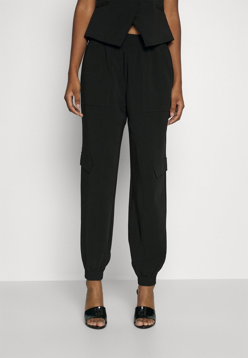 Pantalons cargo noirs avec des chevilles élastiques, comportant des poches latérales et une coupe décontractée. Fabriqués dans un tissu lisse avec une texture subtile.
