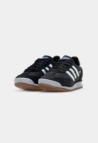Zwarte sneakers met witte strepen en blauwe accenten. Beschikt over een bovenwerk van suede en mesh, een grijze rubberen zool en een gestructureerde gumzool.